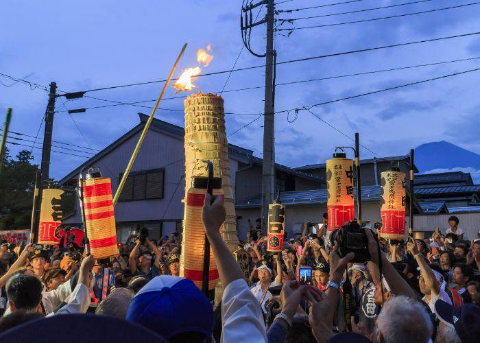 A crowd carrying large paper lanterns and preparing to set fire to a central tower at the Yoshida Fire Festival in Yamanashi.